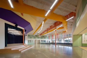 Playful colors shape the stage and cafeteria in a transformed warehouse. Adaptive reuse elementary school. Austin ISD.