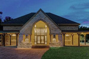 New parish hall glows at night through stone entry porch and covered walkways. Good Shepherd Episcopal, Austin.