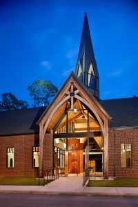 Church entry door illuminated at night. Holy Trinity Episcopal Church, North Carolina by Heimsath Architects.