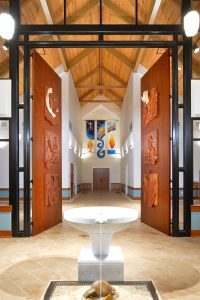 Baptismal font and liturgical art door panels depicting the Holy Trinity. Door carving by artist George Hoelzeman.
