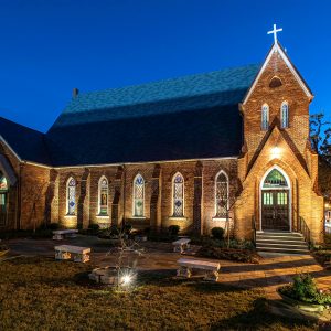 Historic church glowing with night lighting after preservation project completion, by Heimsath Architects.